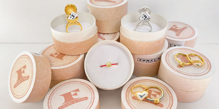 An abundance of ring boxes stacked loosely with Deco Heart Ring, Evil Eye Ring, Fortune Cookie Rings, and Sphere Secret Rings.